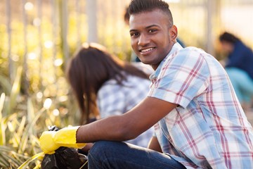 young male crouched down wearing yellow gardening gloves and smiling at the camera