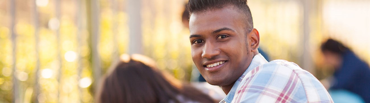 young male crouched down wearing yellow gardening gloves and smiling at the camera