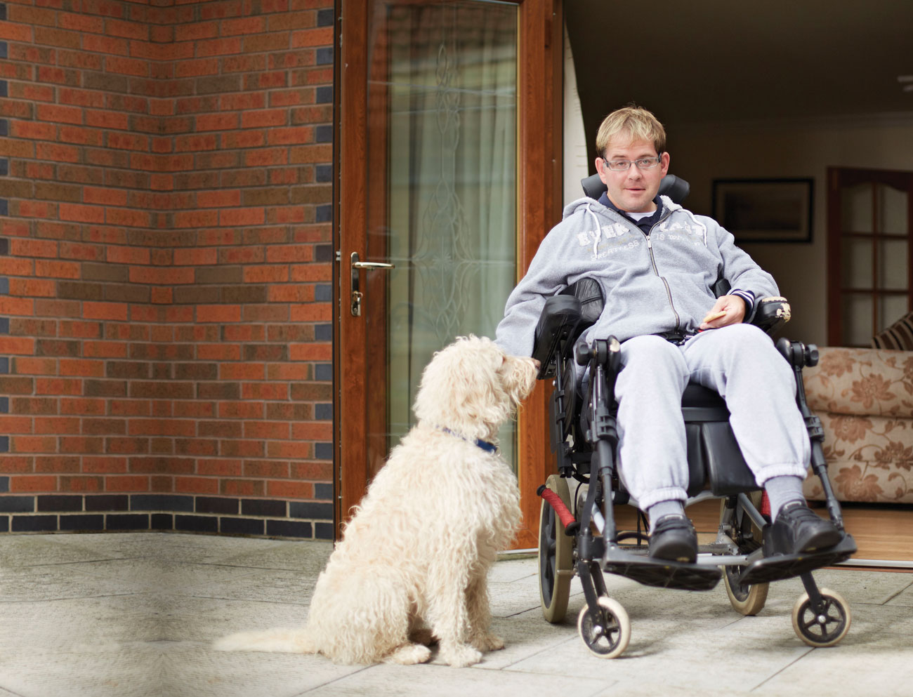 image of a man in wheelchair wearing grey clothing and beside red brick building