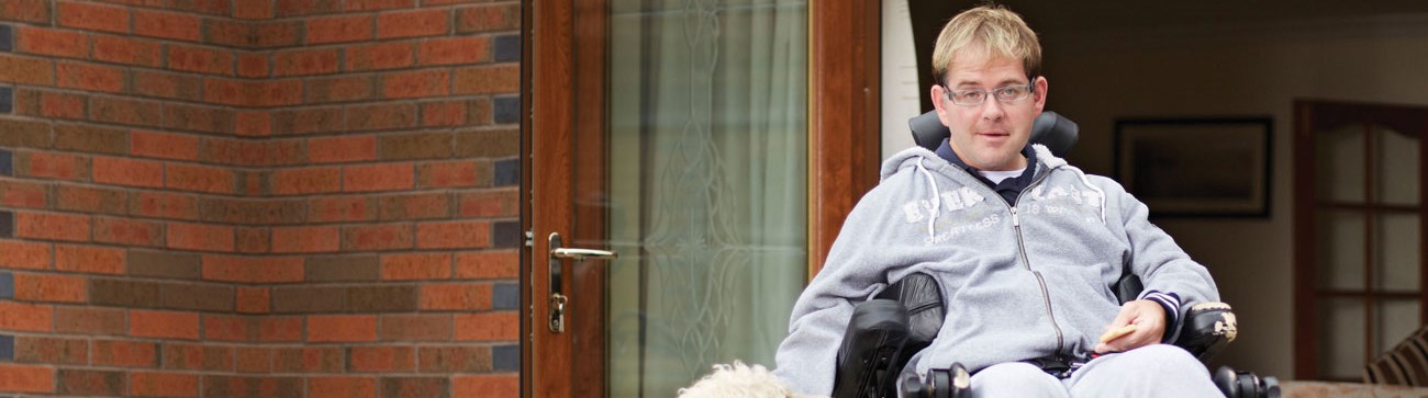 image of a man in wheelchair wearing grey clothing and beside red brick building