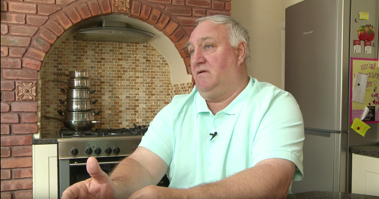a man sat down talking in a kitchen setting, oven visible in background