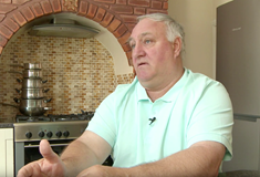 a man sat down talking in a kitchen setting, oven visible in background