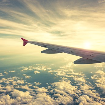 view from an aeroplane, the jet wing in shot with clouds below and sun in the distance