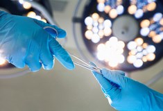 two hands in blue surgical gloves exhanging scissors under operating lights