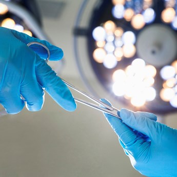 two hands in blue surgical gloves exhanging scissors under operating lights