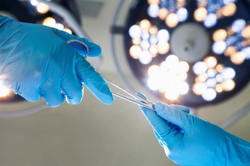 two hands in blue surgical gloves exhanging scissors under operating lights
