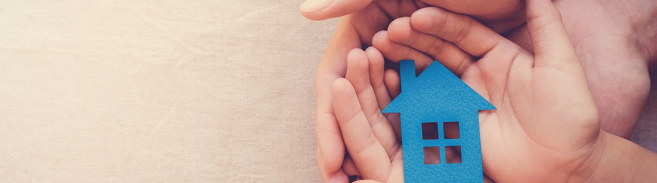 two pairs of hands cupping a small blue house figure