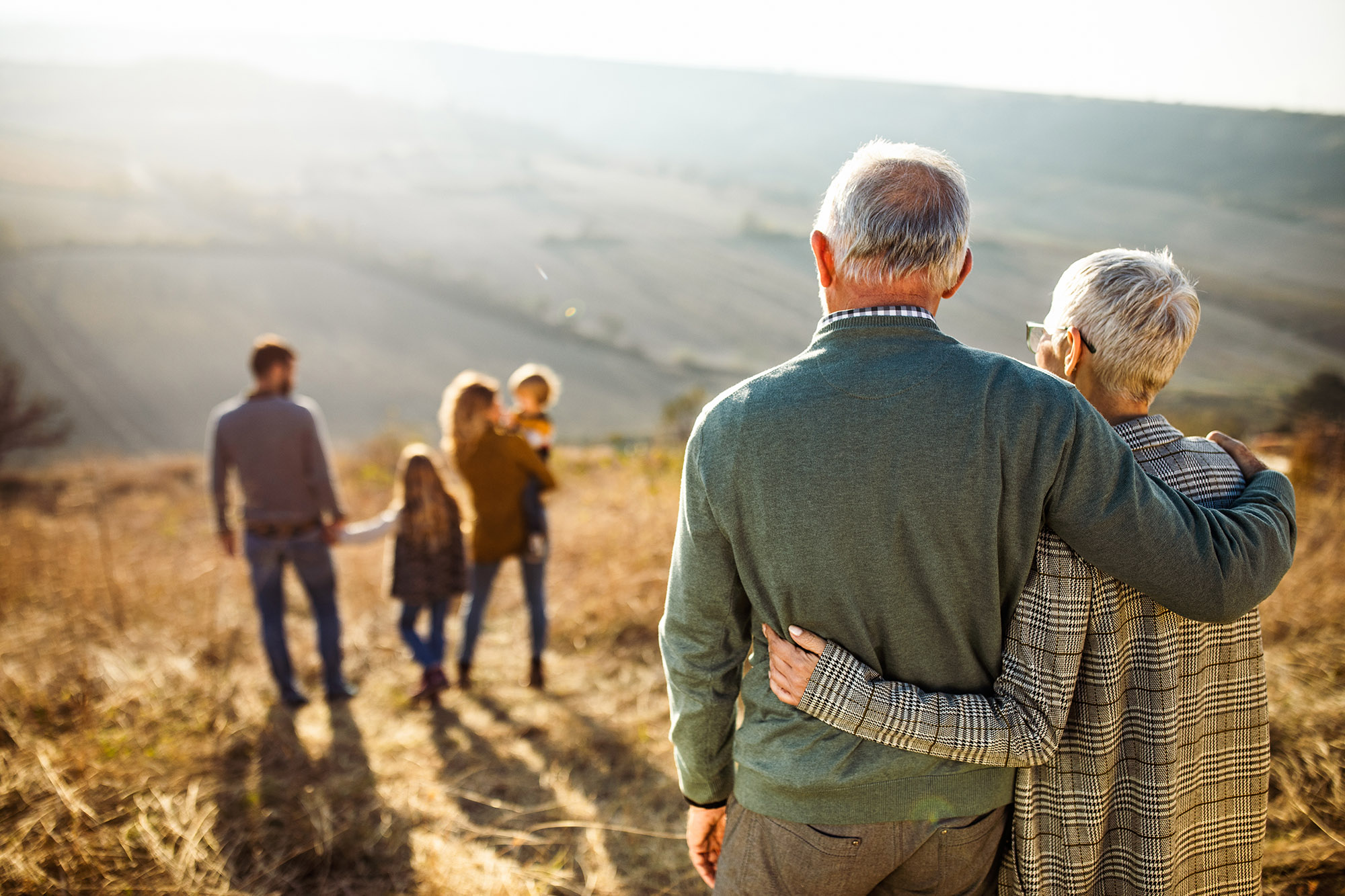 wide shot of elderly couple watching over a younger family of four in the distance