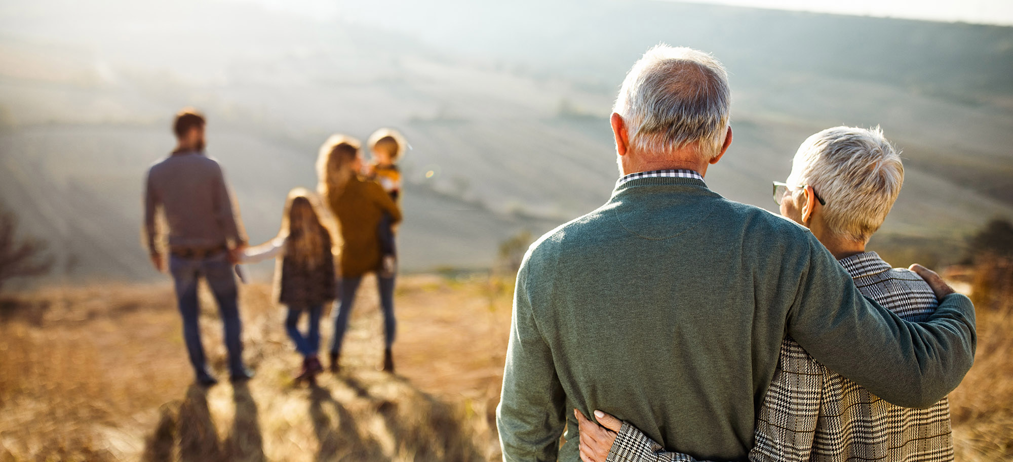 wide shot of elderly couple watching over a younger family of four in the distance