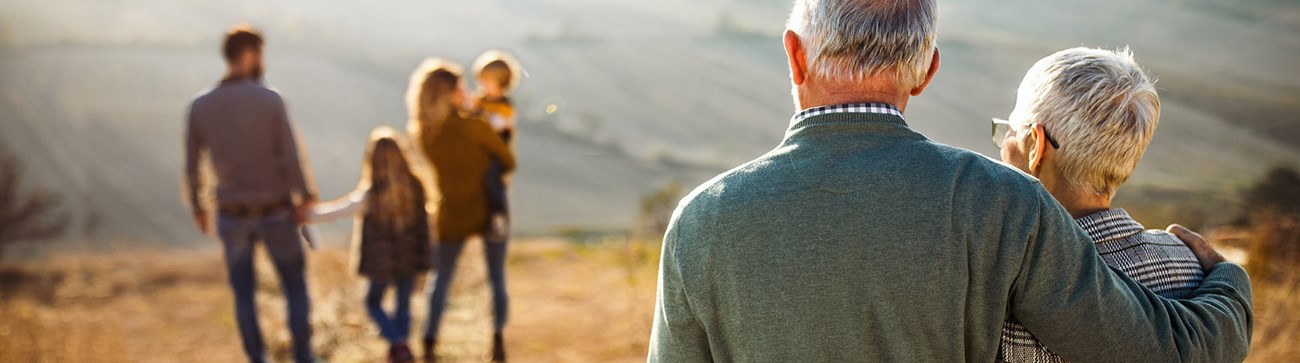 wide shot of elderly couple watching over a younger family of four in the distance