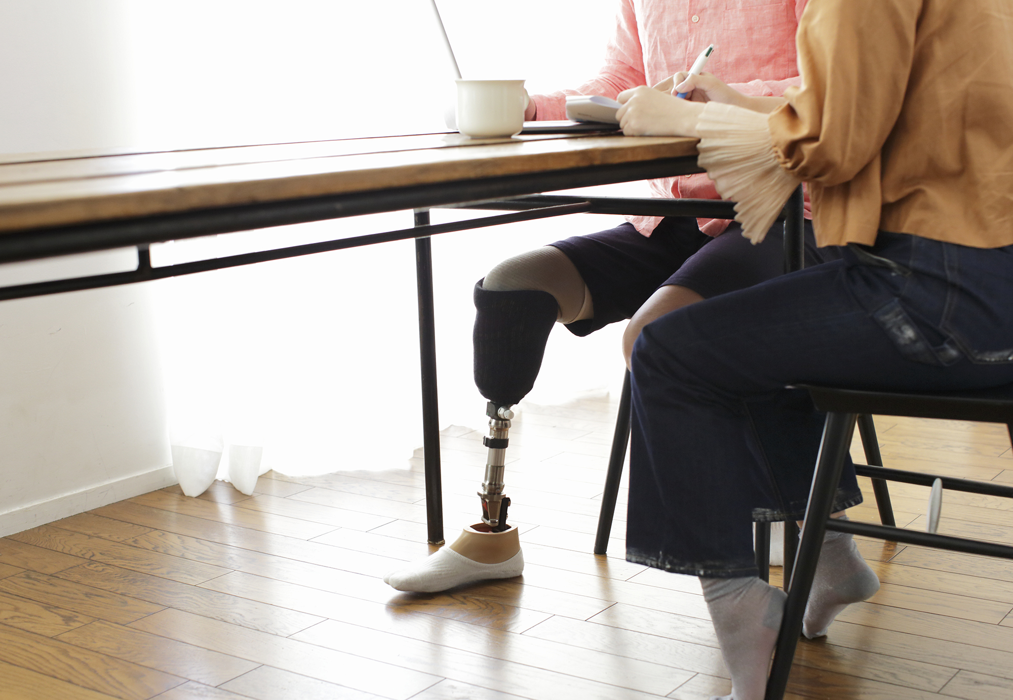 lower body image of two people sitting at a table, one with a prosthetic leg
