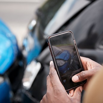 close up of hands holding mobile phone taking a photo of a blue car and a black car which have collided